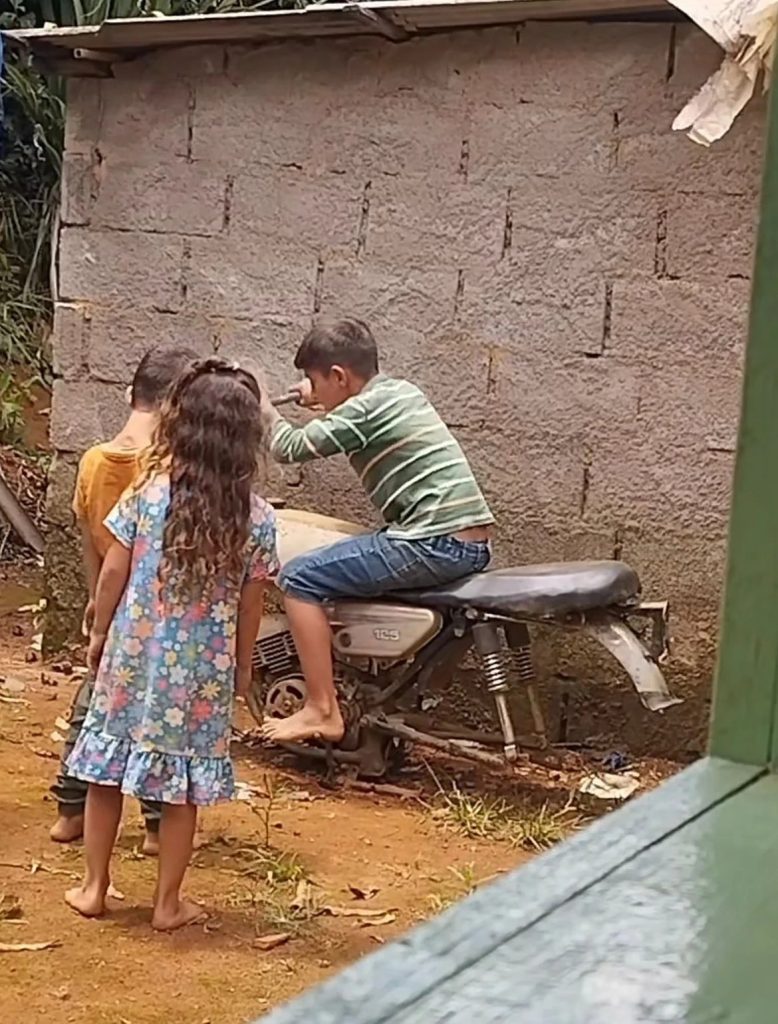 Vídeo mostra três crianças brincando com moto sem rodas em quintal e criatividade diverte internautas nas redes sociais.